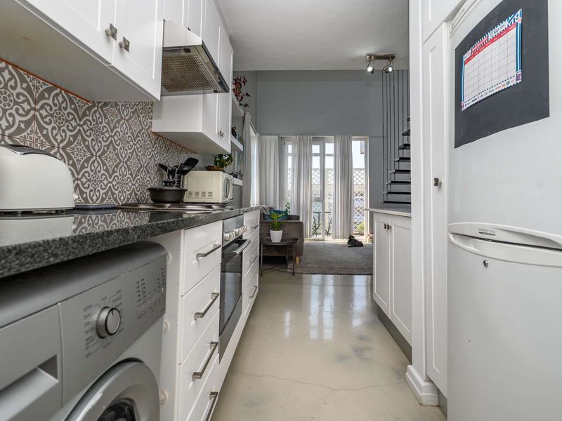 Open-plan kitchen featuring white cabinetry, granite countertops, and patterned tile backsplash, flowing into a living area with access to a balcony.