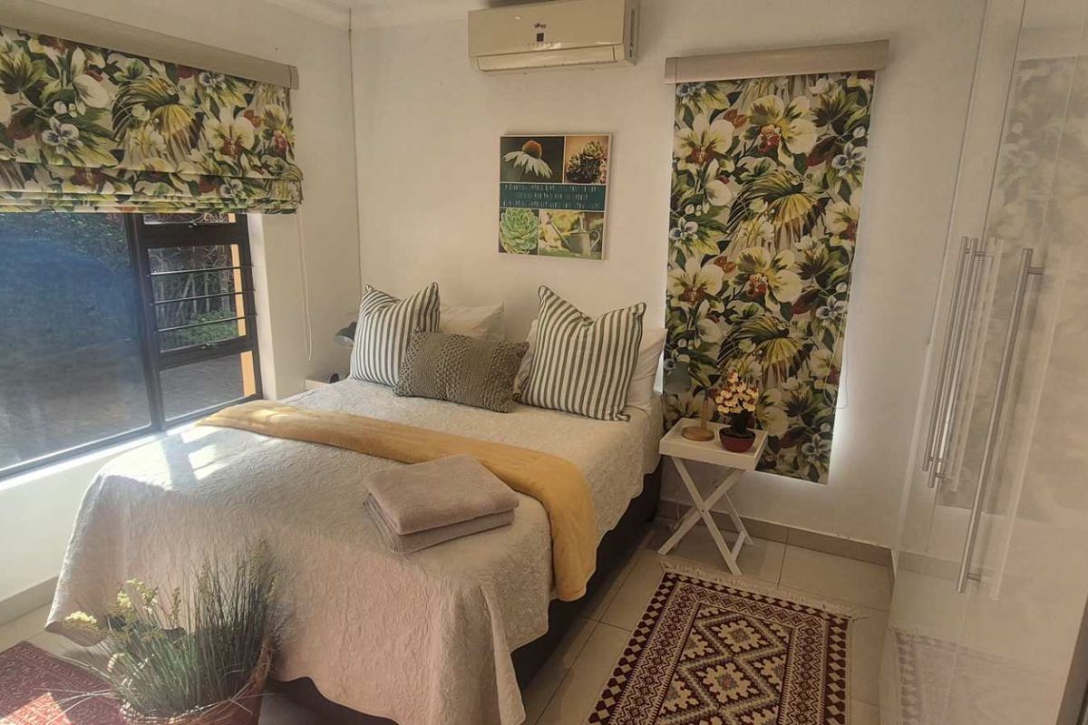 A well-maintained bedroom featuring tiled flooring, a split-system air conditioner, and an integrated shower enclosure, offering a functional and comfortable living space.