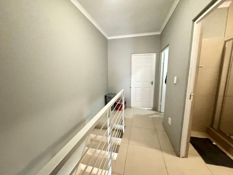 A bright upper-level hallway featuring tiled flooring, a white metal balustrade, and access to adjacent rooms.