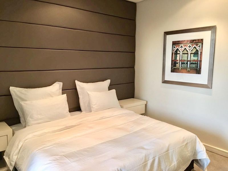 A well-maintained bedroom featuring a large, dark upholstered feature wall panel behind the bed area.
