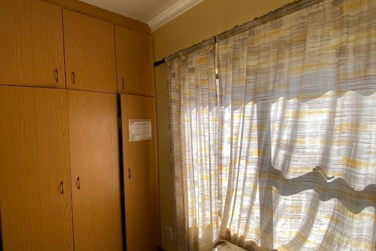 A bedroom featuring built-in wooden cupboards and tiled flooring, providing functional storage space.