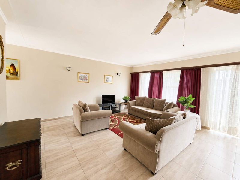 A spacious living room featuring neutral tiled flooring, a ceiling fan, and large sliding glass doors that provide ample natural light.
