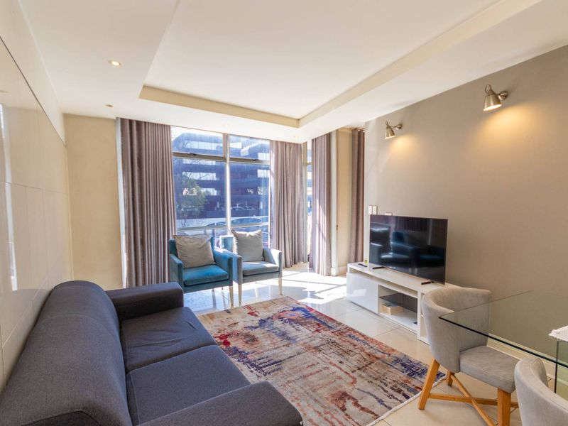 A bright and modern living room featuring tiled floors, recessed ceiling lighting, wall sconces, and large windows providing ample natural light.