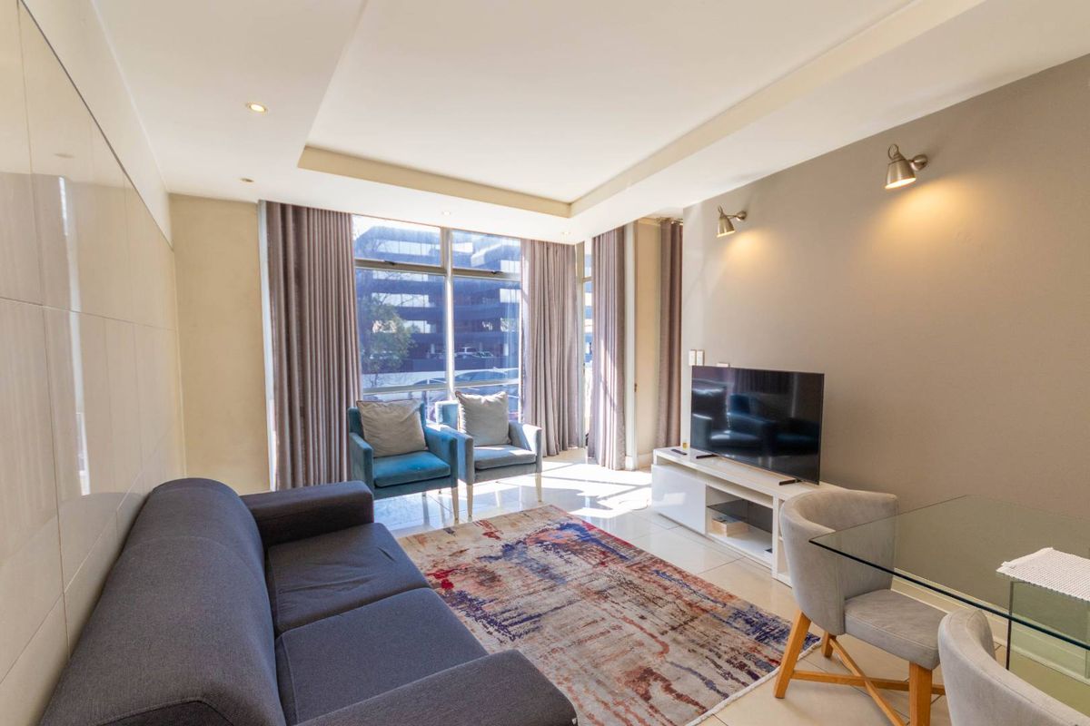 A bright and modern living room featuring tiled floors, recessed ceiling lighting, wall sconces, and large windows providing ample natural light.