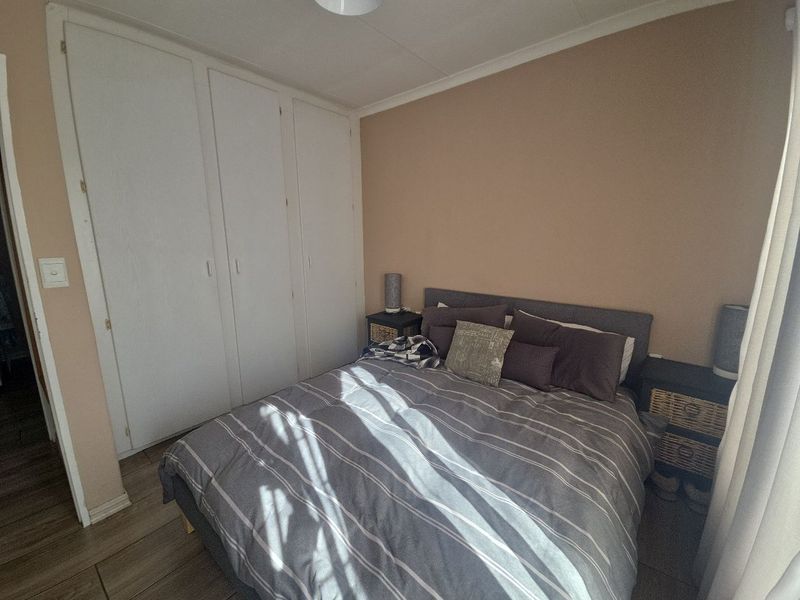 A functional bedroom featuring built-in cupboards, tiled flooring, and neutral wall tones, offering a comfortable and practical living space.