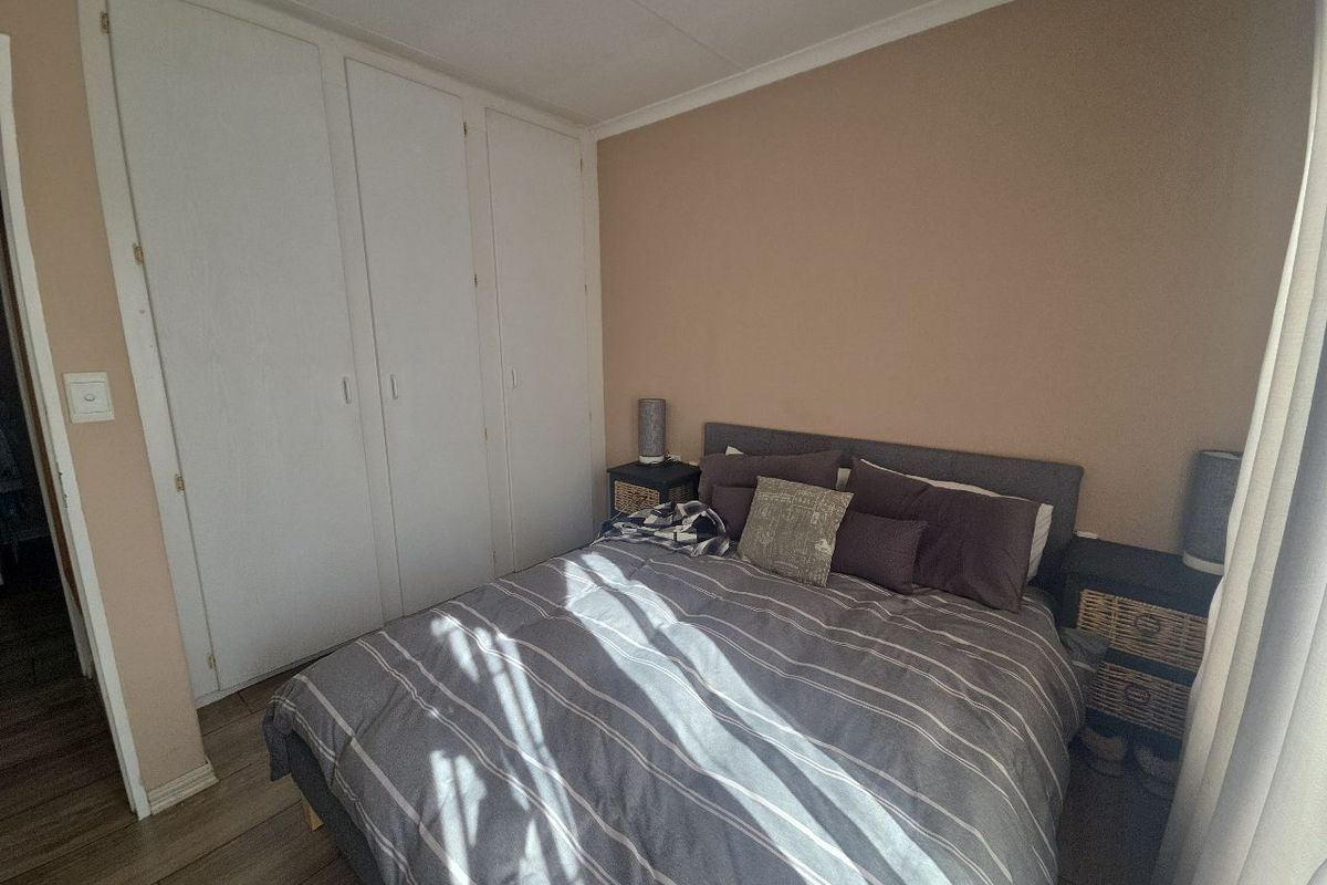 A functional bedroom featuring built-in cupboards, tiled flooring, and neutral wall tones, offering a comfortable and practical living space.