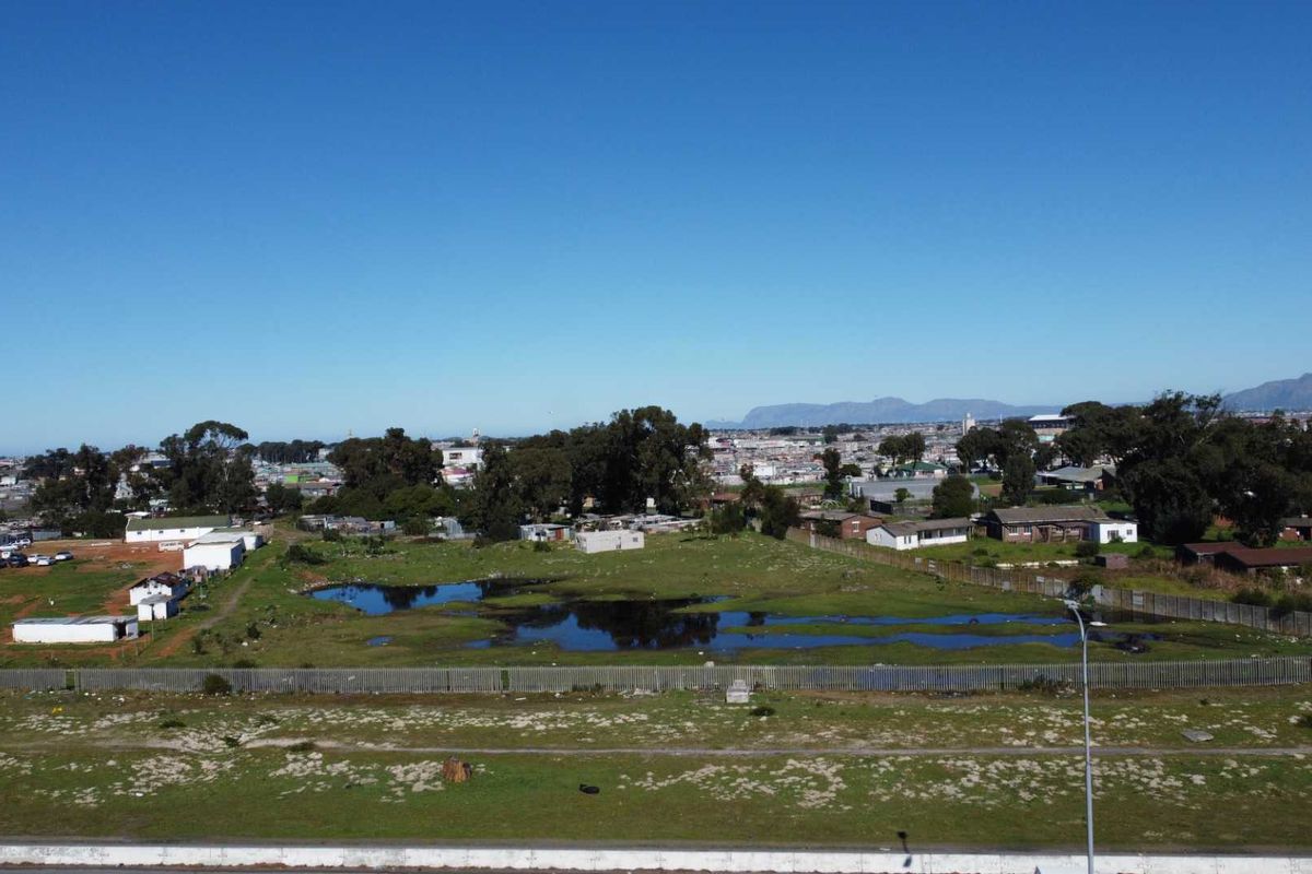 Aerial view of a vacant agricultural plot featuring open land, perimeter fencing, and a natural drainage pond with surrounding residential development.