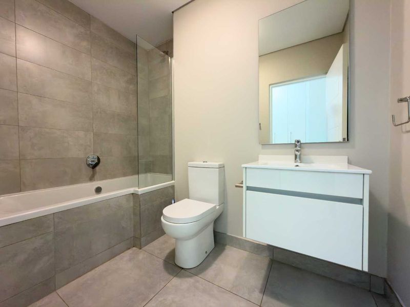 Modern bathroom featuring a built-in bathtub with glass screen, wall-mounted vanity with basin, and neutral large-format floor and wall tiling.