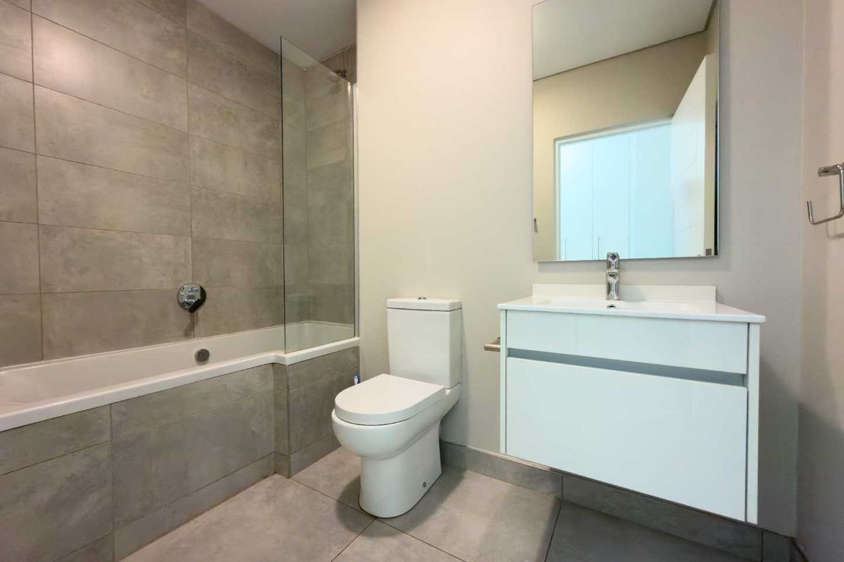 Modern bathroom featuring a built-in bathtub with glass screen, wall-mounted vanity with basin, and neutral large-format floor and wall tiling.