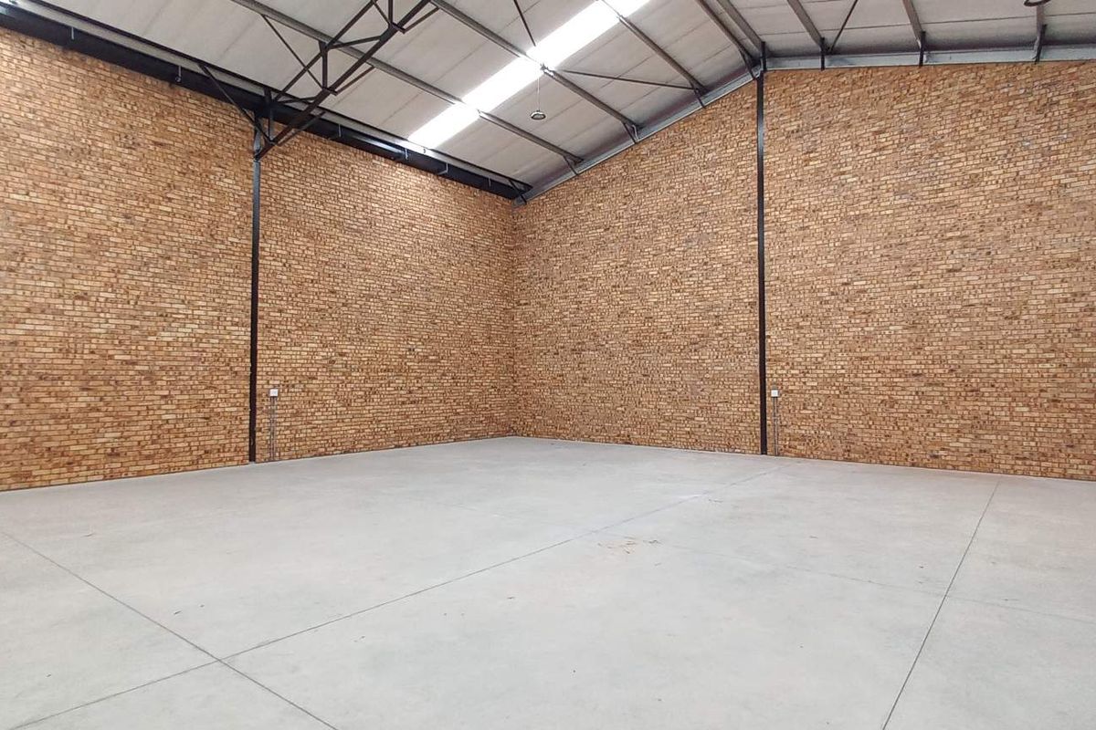 Spacious industrial warehouse unit featuring high ceilings with exposed steel trusses, durable concrete flooring, and attractive face-brick walls.