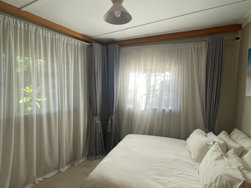 A well-lit bedroom featuring neutral tiled flooring, clean wall finishes, and floor-to-ceiling curtain treatments.