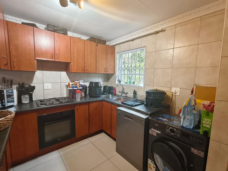 A functional kitchen featuring wooden cabinetry, tiled backsplash, built-in oven and hob, and tiled flooring with a window overlooking the exterior.