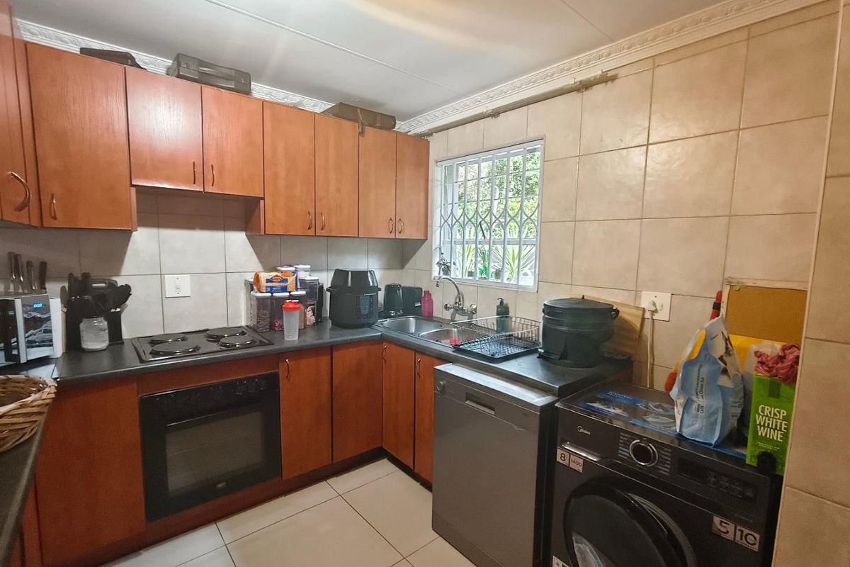 A functional kitchen featuring wooden cabinetry, tiled backsplash, built-in oven and hob, and tiled flooring with a window overlooking the exterior.