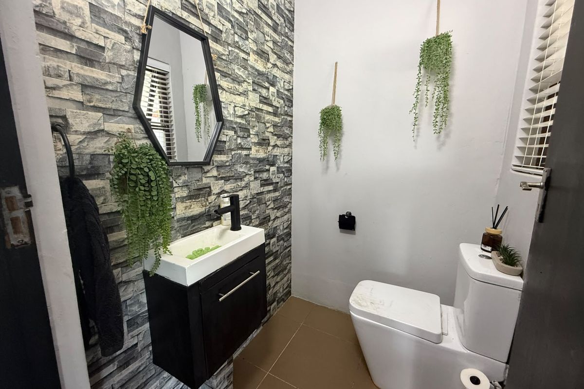 A compact bathroom featuring a stone-cladding accent wall, wall-mounted vanity with basin, and modern toilet with tiled flooring.