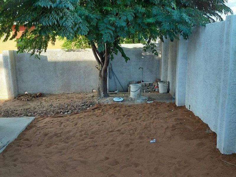 A private rear garden area featuring a perimeter boundary wall, a mature tree, and an outdoor water tap, currently awaiting landscaping.