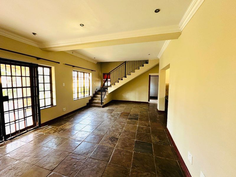Spacious open-plan living area featuring slate tile flooring, a central staircase with metal railing, and abundant natural light through large grid-pattern windows.