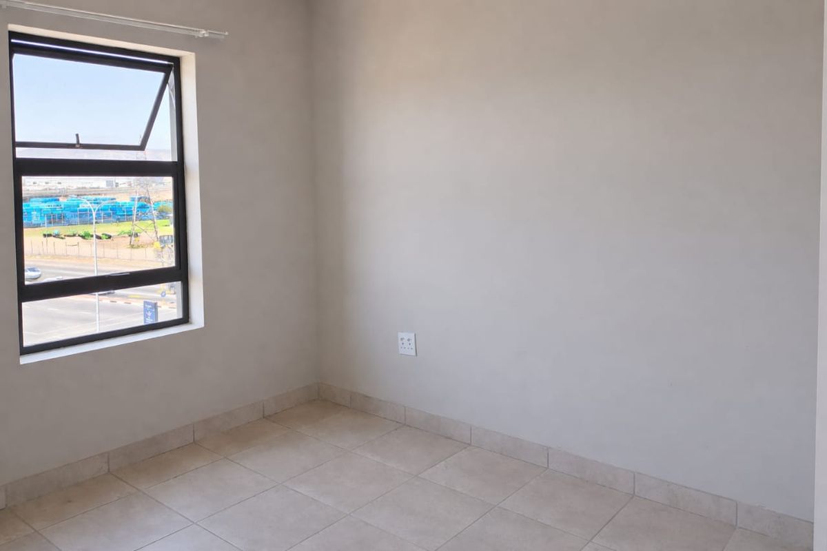 A bright, empty bedroom featuring neutral tiled flooring, a large window with exterior views, and clean, minimalist wall finishes.