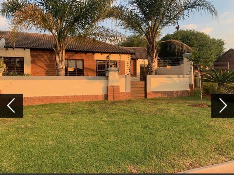 Front view of a single-story brick house featuring a tiled roof, perimeter wall with electric fencing, and a well-maintained front lawn.