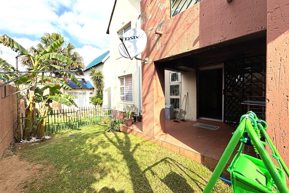Rear view of the townhouse featuring a covered patio, small private garden area, and exterior wall finishes.