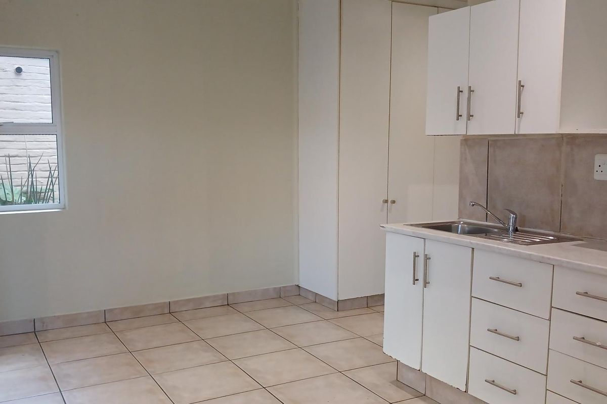 A functional kitchen area featuring white cabinetry, tiled flooring, and a stainless steel sink, offering a clean and practical space.