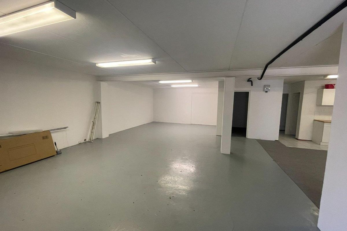 An open-plan commercial space featuring painted concrete flooring, structural columns, and functional overhead fluorescent lighting, suitable for various business or office configurations.
