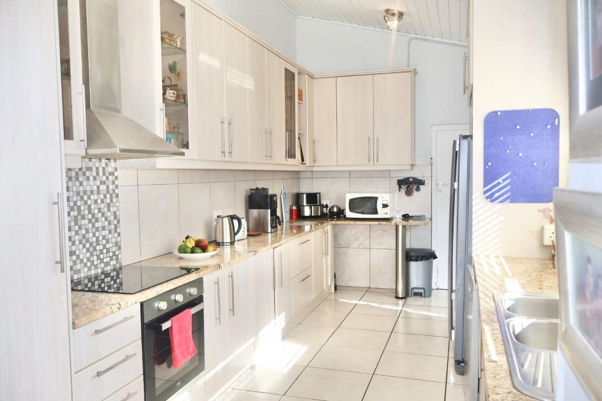 A functional kitchen featuring light-toned cabinetry, granite countertops, a built-in oven, glass cooktop, stainless steel extractor fan, and tiled flooring.