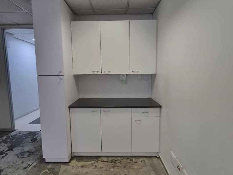 A small utility or kitchenette area featuring white built-in cabinetry, a dark countertop, and a drop ceiling, currently requiring flooring repairs.