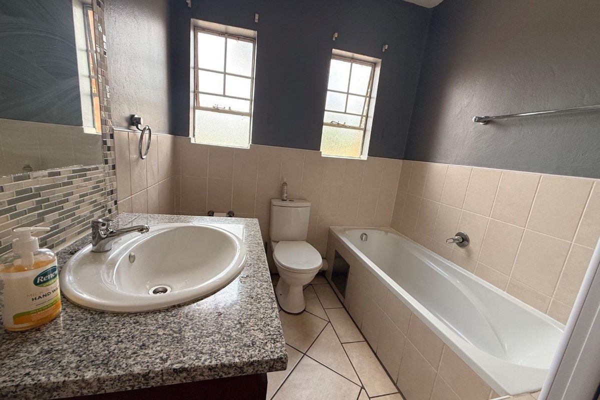 A functional bathroom featuring a built-in bathtub, a vanity with a granite countertop, a toilet, and tiled wall finishes.