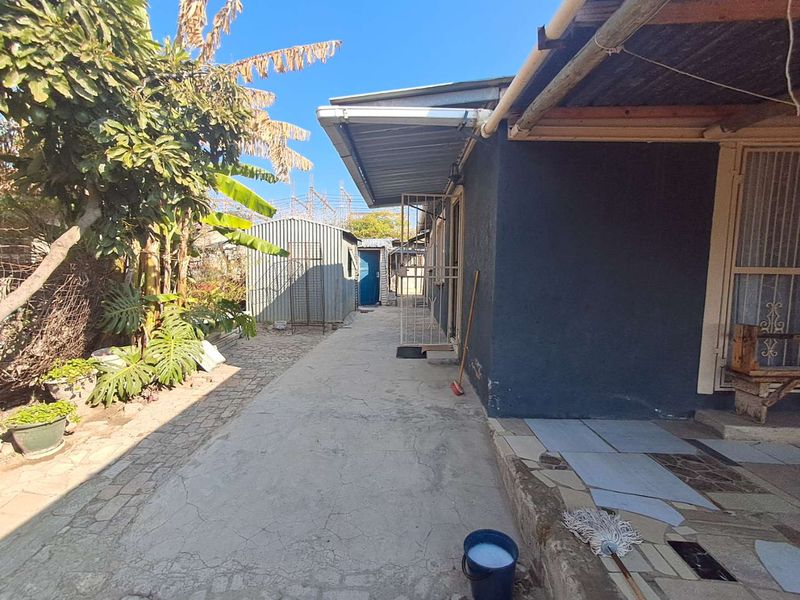 A rear exterior view showing a concrete pathway, covered walkway, and a detached metal storage shed in the garden area.