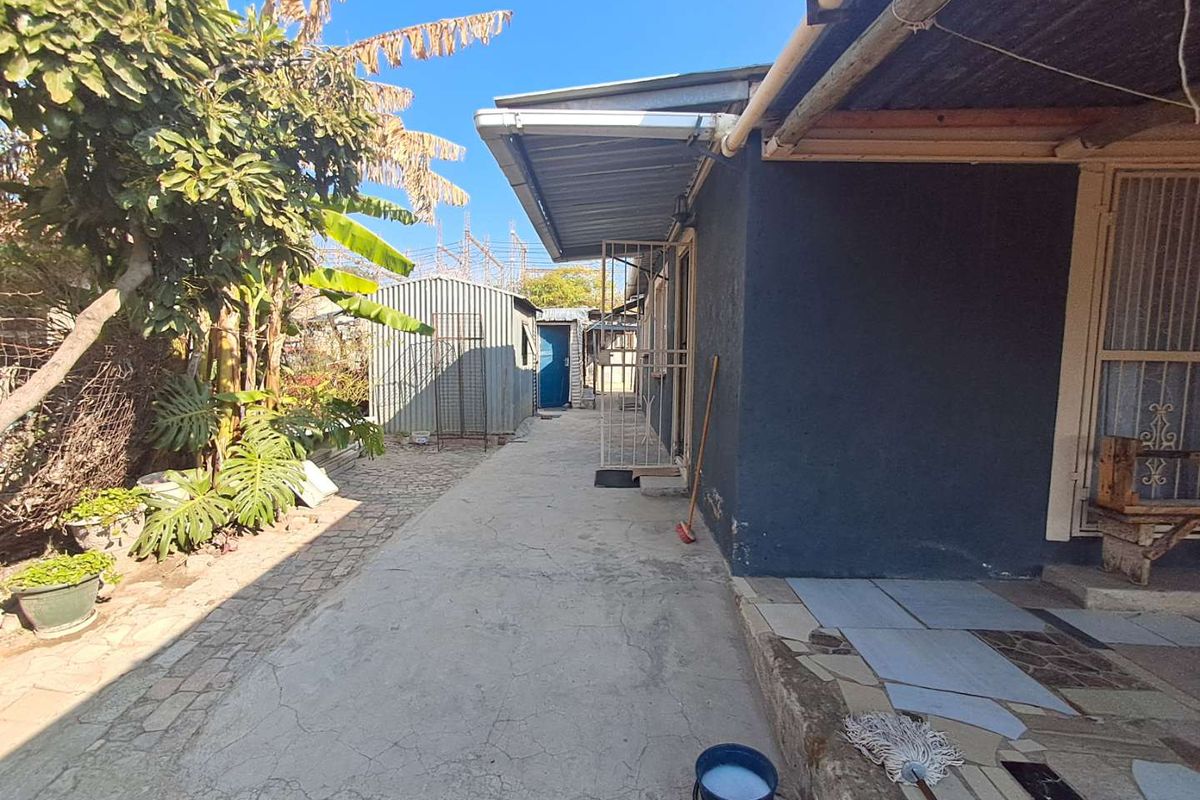 A rear exterior view showing a concrete pathway, covered walkway, and a detached metal storage shed in the garden area.
