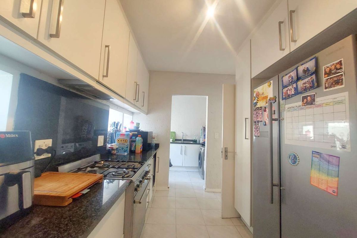 A functional kitchen featuring granite countertops, built-in cabinetry, a gas hob, and an extractor fan, with an adjacent scullery area.
