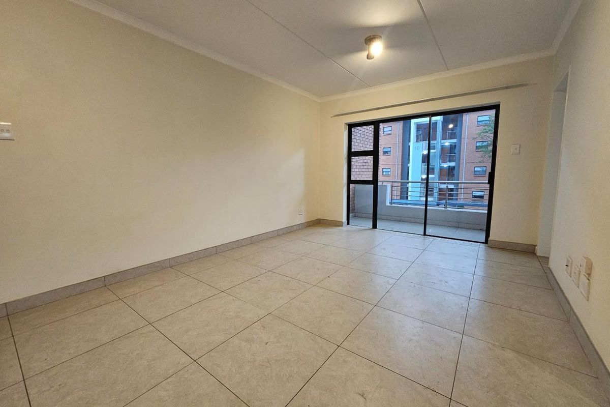 A bright, empty living area featuring neutral floor tiles, coved ceilings, and large sliding glass doors that open onto a private balcony.