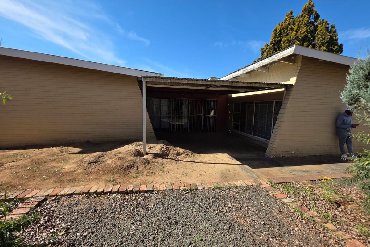 Rear exterior view of the house featuring a covered patio area, brick facade, and security gates, with an unfinished garden space.