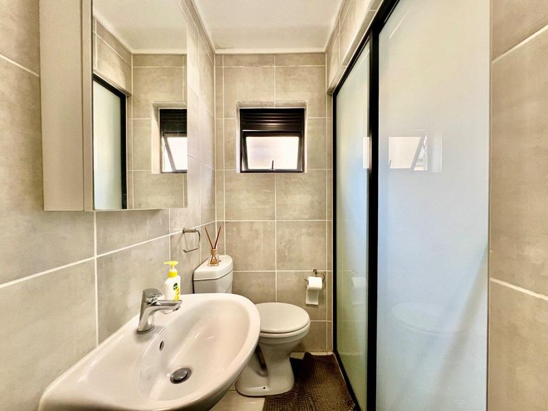A modern, well-maintained bathroom featuring neutral ceramic tiling, a pedestal basin, a toilet, and a glass-enclosed shower.