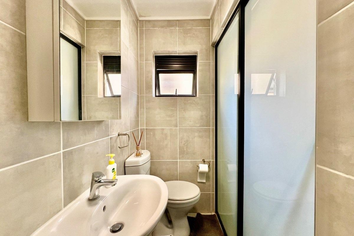 A modern, well-maintained bathroom featuring neutral ceramic tiling, a pedestal basin, a toilet, and a glass-enclosed shower.
