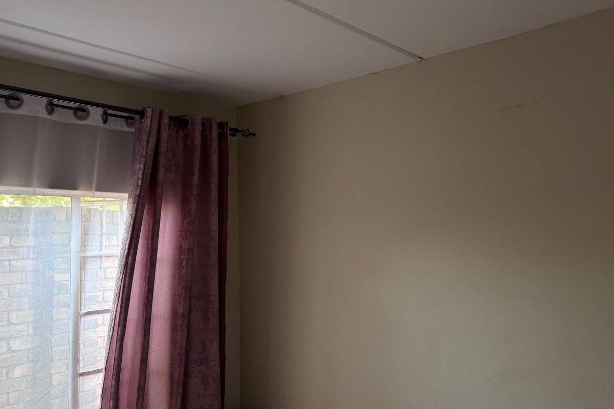 A view of a bedroom corner featuring a window with a curtain rod and neutral wall finishes.