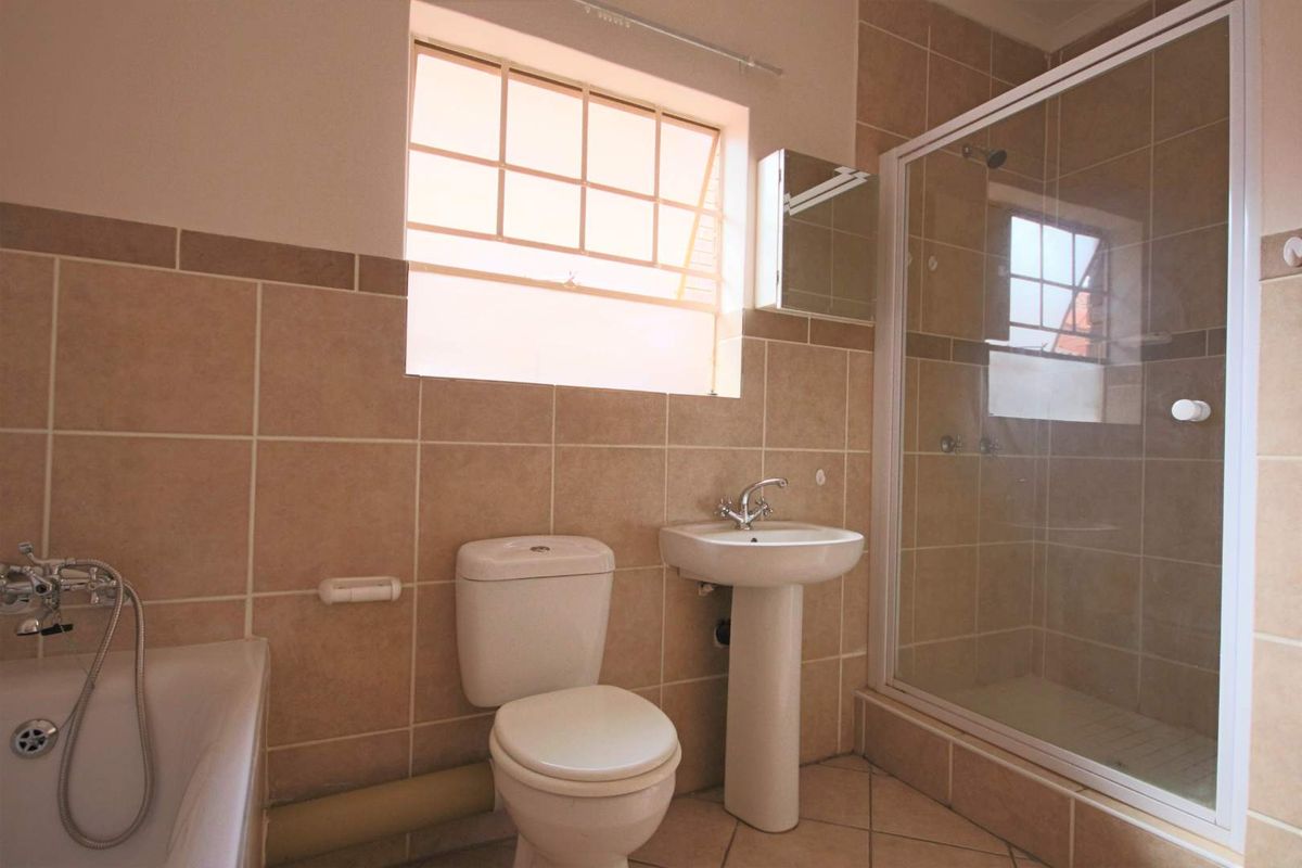 A clean, functional bathroom featuring a separate bathtub, glass-enclosed shower, pedestal sink, and neutral wall tiling.