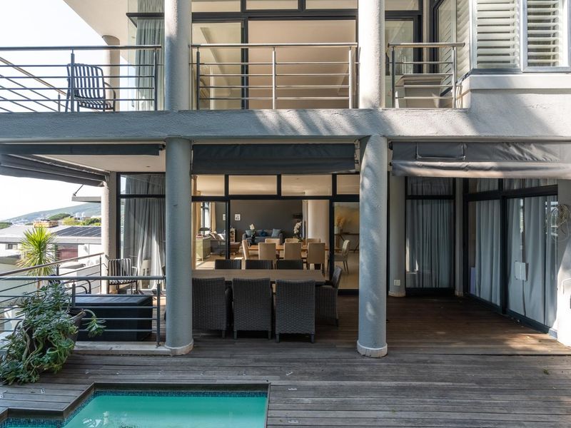 Spacious multi-level patio featuring timber decking, a swimming pool, and stainless steel balustrades, providing seamless indoor-outdoor flow through large sliding glass doors.