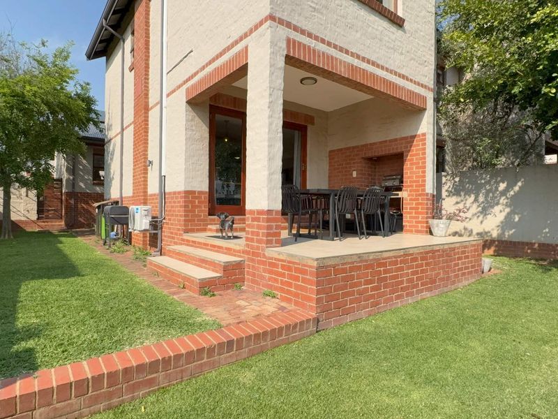 Rear view of the townhouse featuring a covered brick patio with a built-in braai, overlooking a private garden with a lawn.