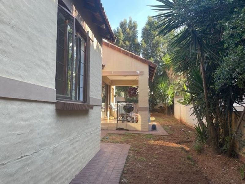 Rear view of the property showing a covered patio, paved walkway, and established garden area with boundary walling.