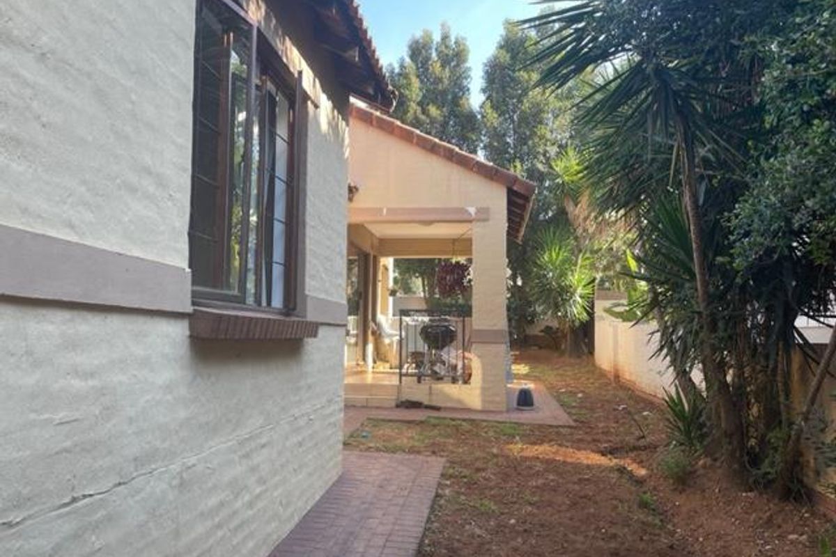 Rear view of the property showing a covered patio, paved walkway, and established garden area with boundary walling.