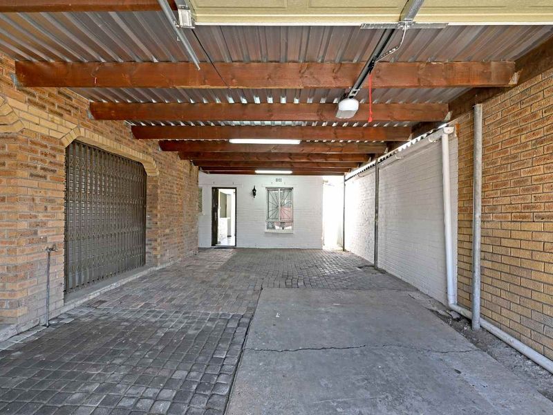 A covered, paved garage area featuring exposed timber beams, brick walls, and secure gated access, providing functional vehicle storage space.