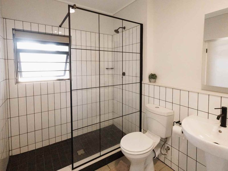 Modern bathroom featuring a walk-in shower with a black-framed glass screen, pedestal basin with black fixtures, and clean white wall tiling.
