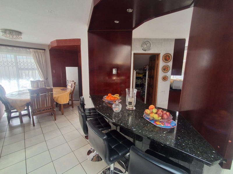 Open-plan living and dining area featuring a granite breakfast bar, tiled flooring, and direct access to a scullery.