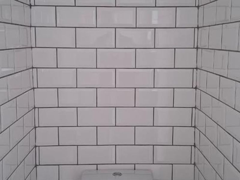 A compact, clean bathroom featuring modern white subway wall tiles and a standard toilet fixture.
