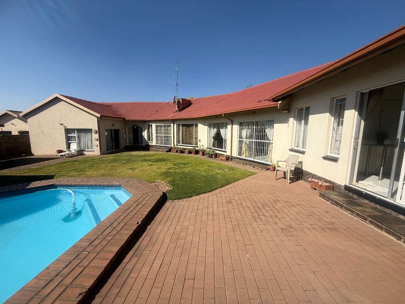 Rear exterior view featuring a paved patio area, a swimming pool, and access to the home via multiple sliding doors.