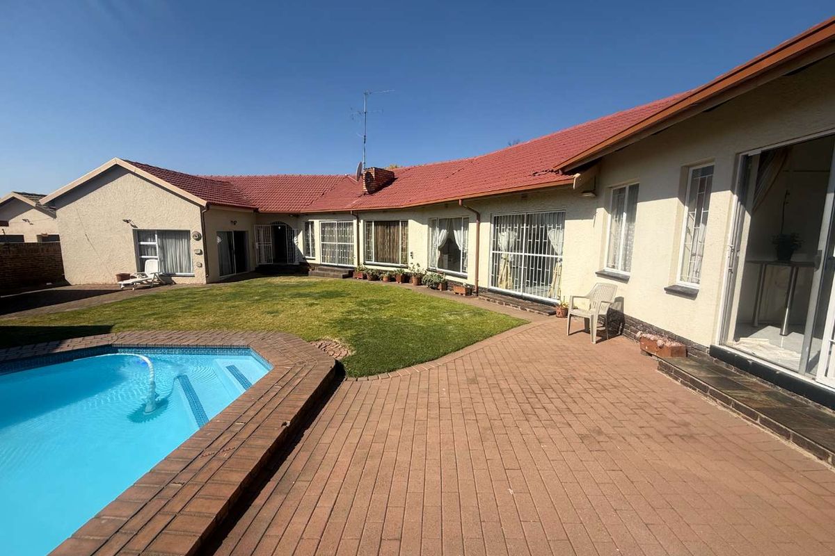Rear exterior view featuring a paved patio area, a swimming pool, and access to the home via multiple sliding doors.
