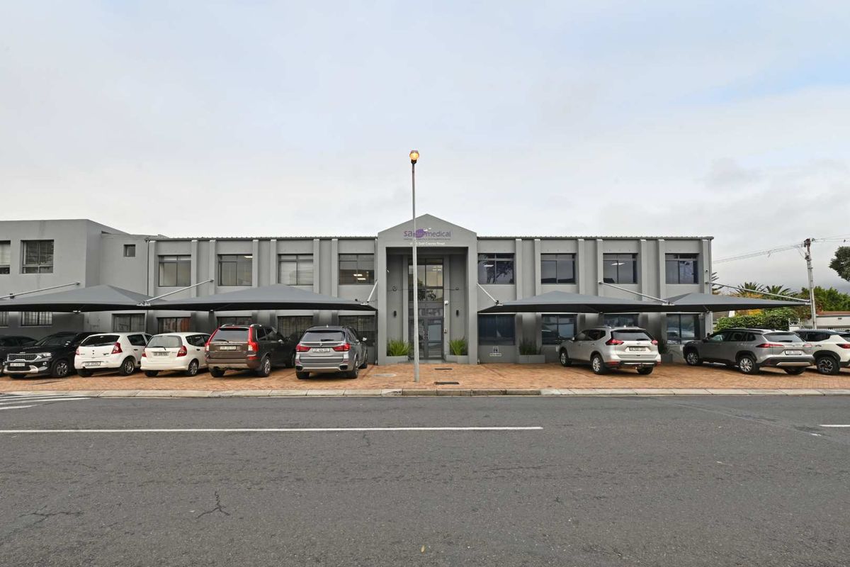 Front elevation of a commercial medical facility featuring a paved parking area with shade cloth carports and a modern multi-story facade.