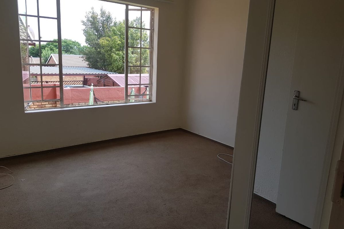 A vacant bedroom featuring a large window with metal frames and carpeted flooring, offering a blank canvas for potential interior updates.