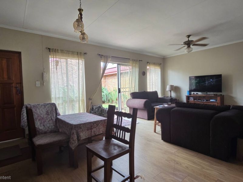 A spacious living room featuring laminate flooring, a ceiling fan, and sliding glass doors that provide access to the outdoor area.